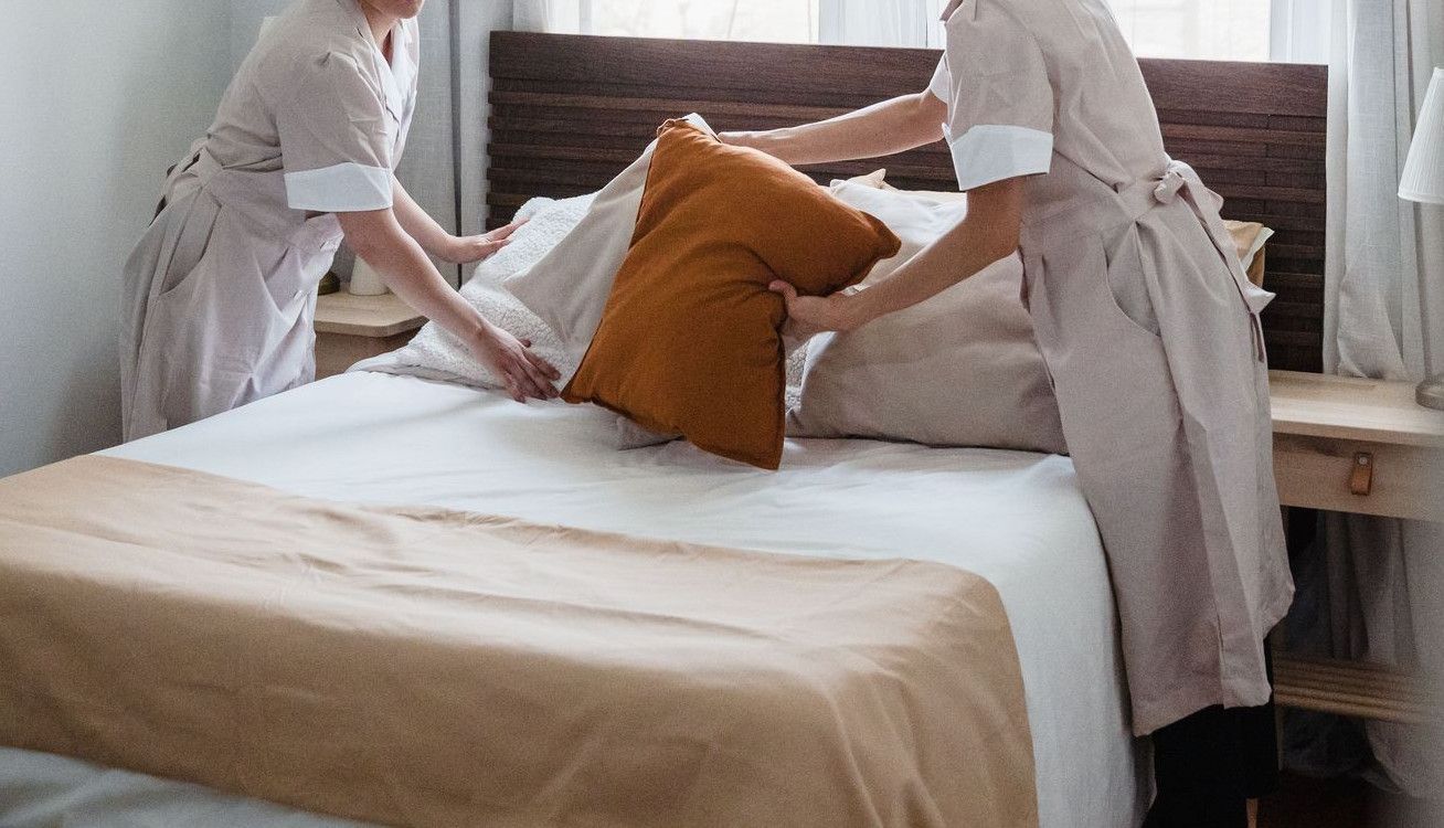 Two housekeepers organizing bed linen in a bright, cozy bedroom.
